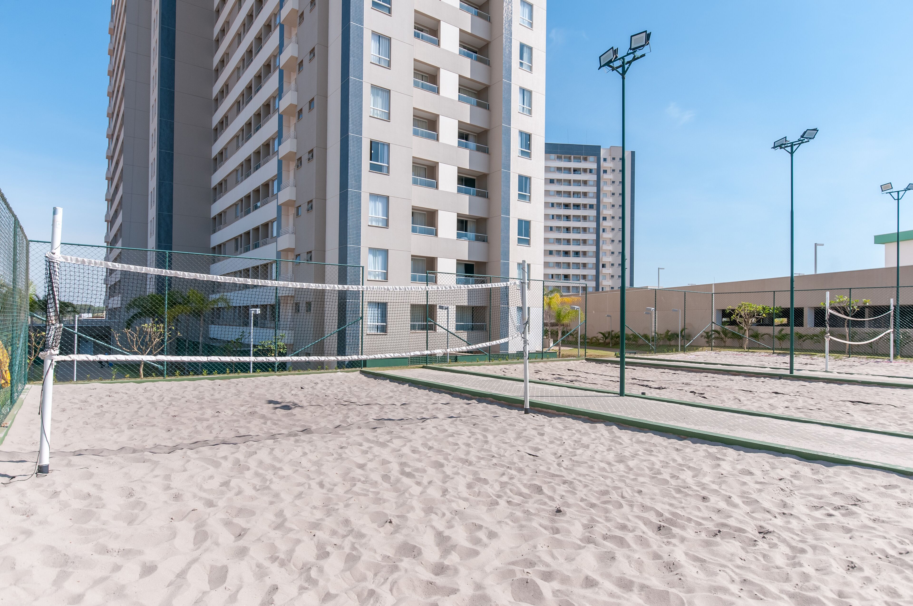 Un terrain de beach-volley sablonneux, avec un filet, entouré de grands immeubles et d’éclairages publics.