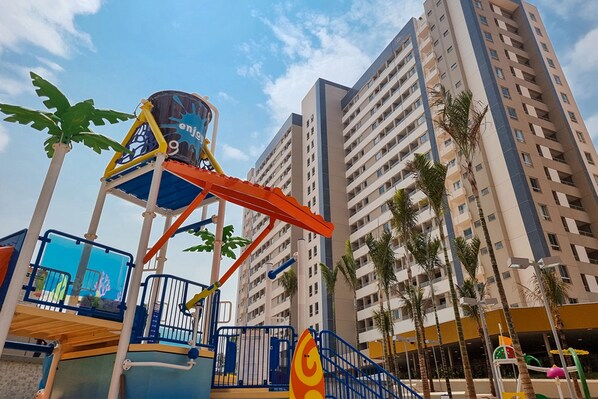 A water park with a water slide and play structures, surrounded by tall residential buildings. - Enjoy Solar das Águas Park Resort (Olímpia)