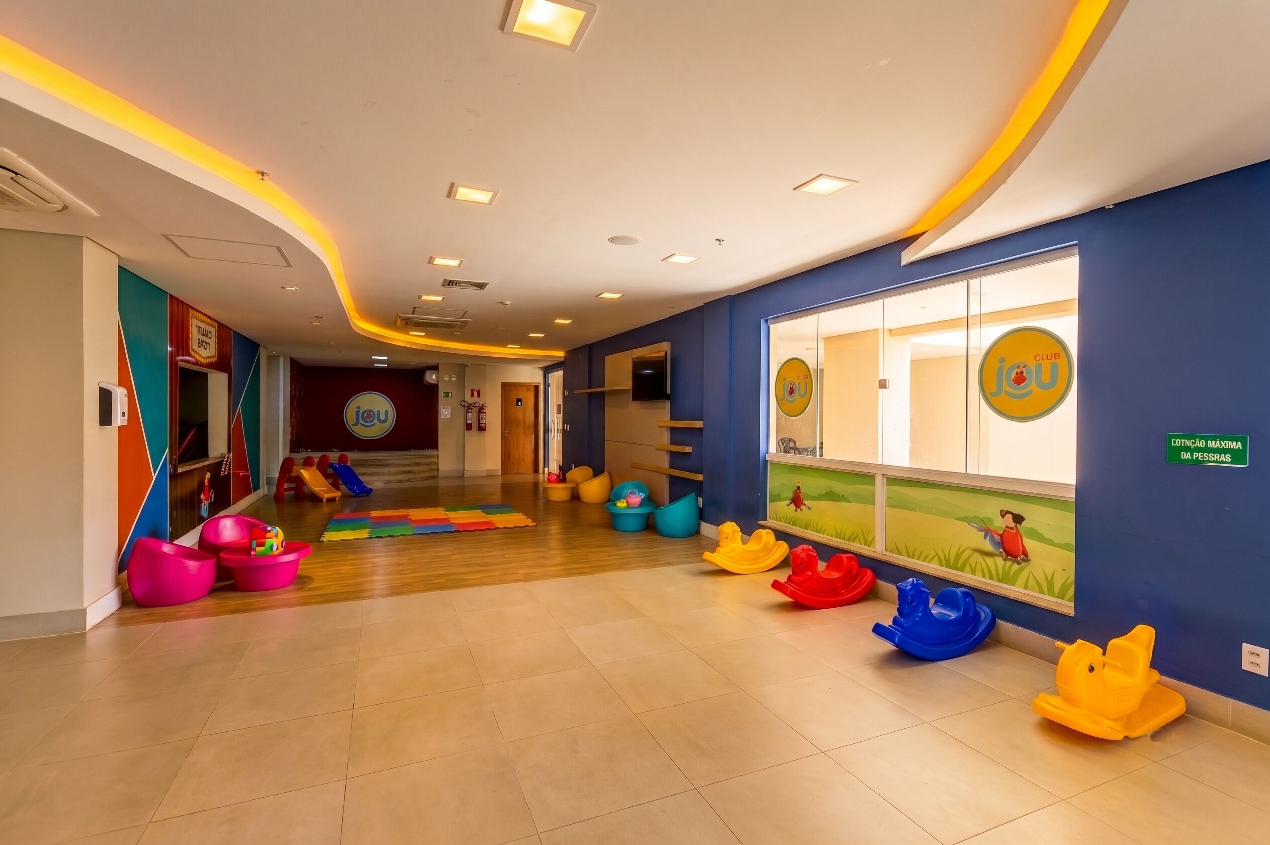 Un espacio interior bien iluminado con área de juegos, asientos coloridos y un mural en la pared.