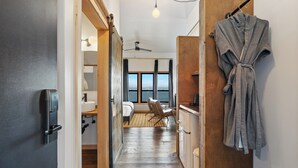 A narrow hallway leading to a bedroom with a view of the sea, a wooden floor, a robe hanging on the wall, and a ceiling fan. - Bowline Hotel (Astoria)