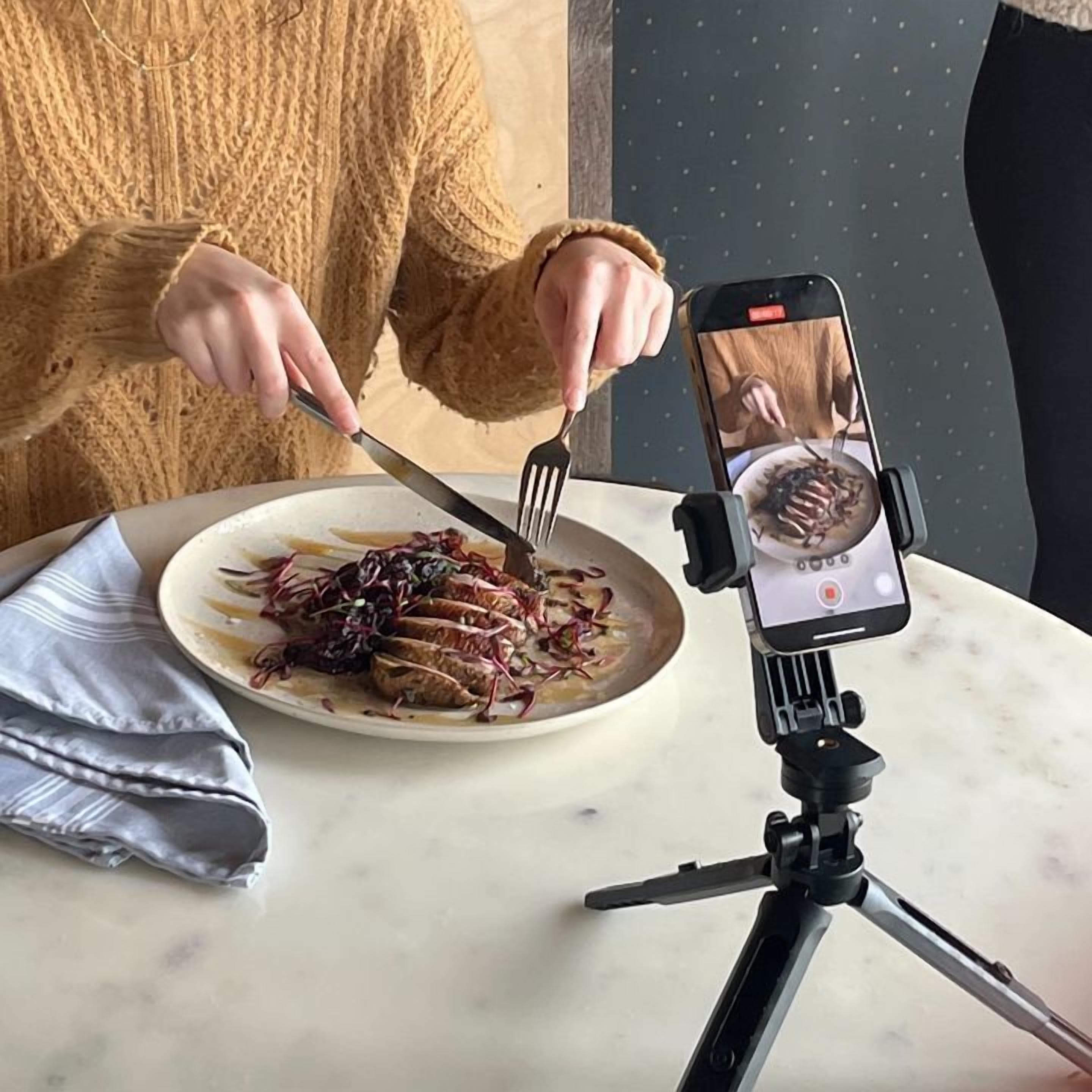 Una persona comiendo en una mesa con un teléfono inteligente sujeto a un trípode, grabando la comida.