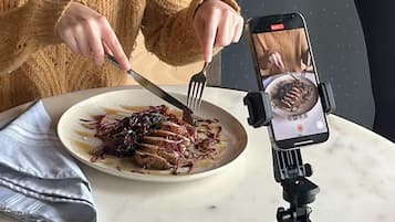 Una persona comiendo en una mesa con un teléfono inteligente sujeto a un trípode, grabando la comida.