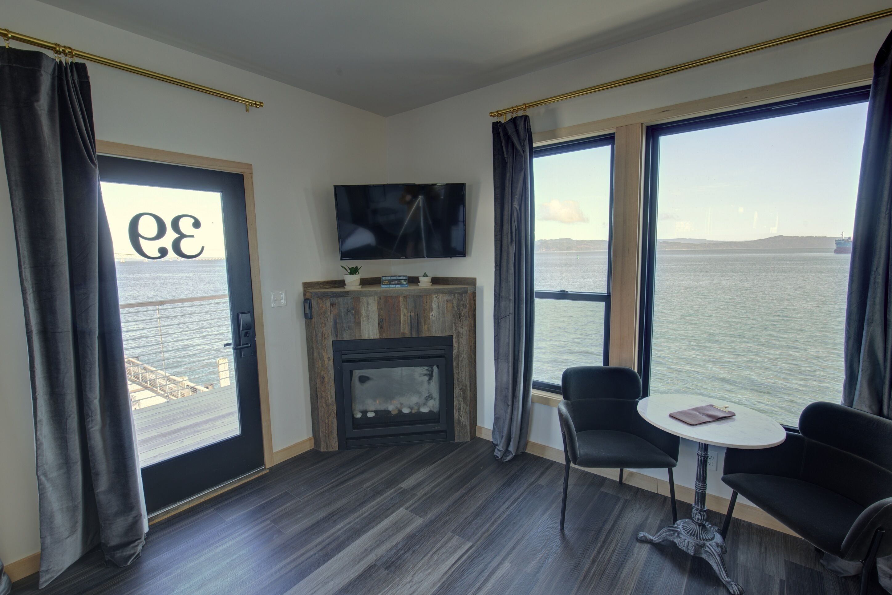 A modern room with a fireplace, a TV, and large windows overlooking a body of water.