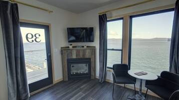 A modern room with a fireplace, a TV, and large windows overlooking a body of water.