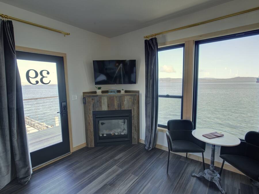 A modern room with a fireplace, a TV, and large windows overlooking a body of water.