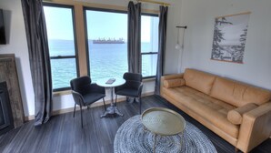 Een woonkamer met een groot raam, een bank, twee stoelen, een bijzettafeltje en een decoratief object aan de muur.