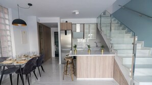 Une cuisine moderne dotée d’un îlot central, d’un coin repas avec une table en verre et d’un escalier avec des rampes en verre.