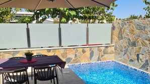 Un espace aménagé au bord de la piscine, avec une table et des chaises, un mur en pierre et une piscine à l’eau d’un bleu limpide.