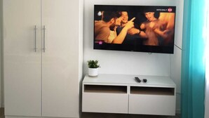A modern living room with a white TV on a wall, a white cabinet, and a small plant on the cabinet. - LouVi Apartment in Kehl am Rhein (Kehl)