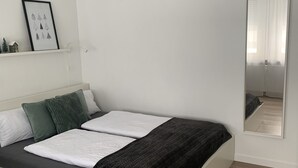 A modern bedroom with a white bed, green and white pillows, a framed picture on the wall, and a large mirror. - LouVi Apartment in Kehl am Rhein (Kehl)
