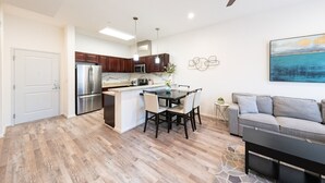 Una cocina moderna con una isla central, armarios de madera oscura, electrodomésticos de acero inoxidable y un área de comedor con un sofá gris y una mesa de centro.