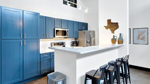 Una cocina moderna con armarios azules, un bote de basura de acero inoxidable y una barra con taburetes.
