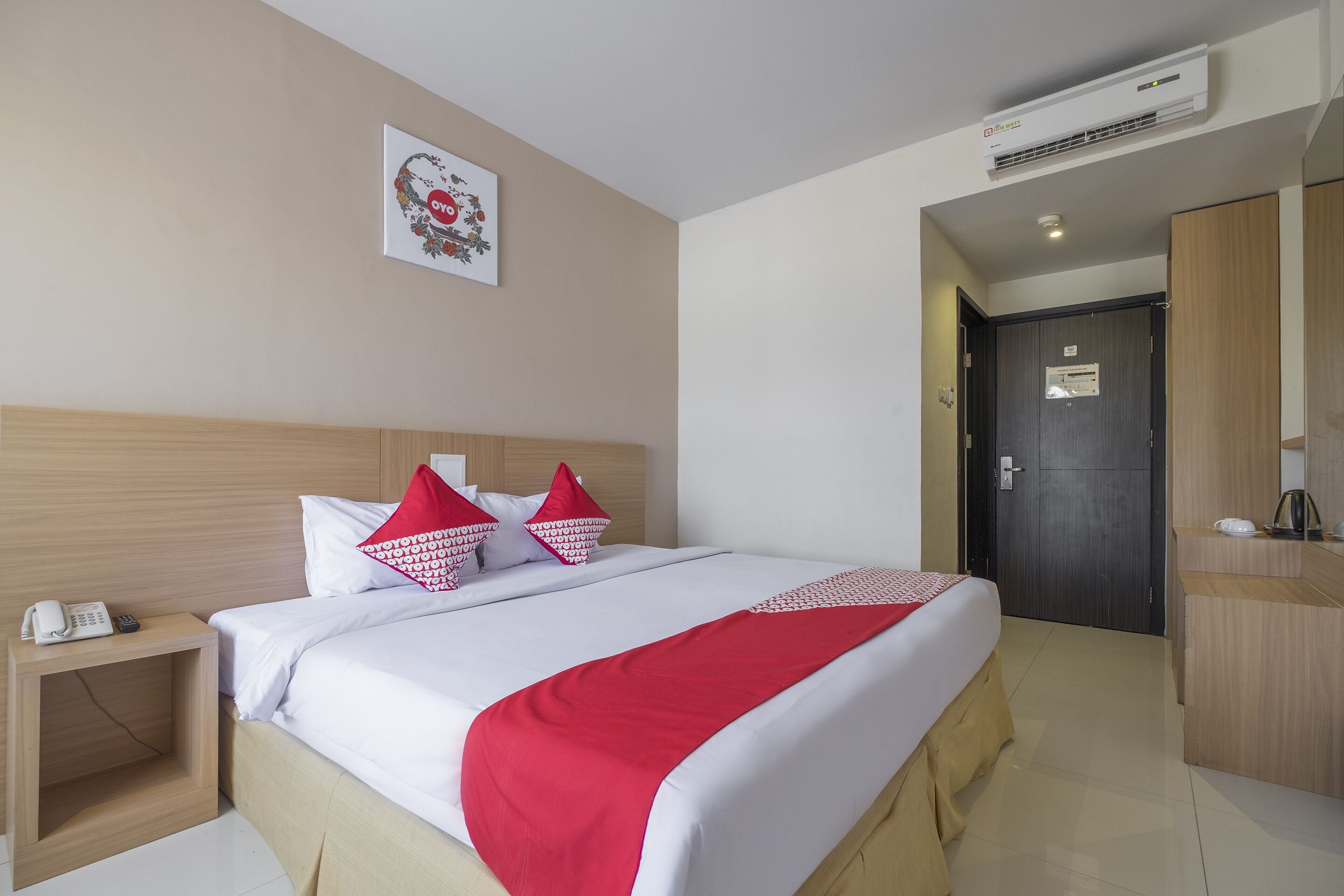 A hotel room with a bed, bedside table, and a wall-mounted air conditioner.