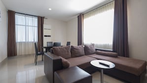 A modern living room with a sectional sofa, a small round table, and a dining area with a table and chairs. - All Nite and Day Makassar (Makassar)