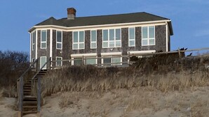 A two-story house with a large front porch and a staircase leading to the entrance. - Oceanfront w/Private Stairs to Beach and Spectacular Sunsets! (Eastham)