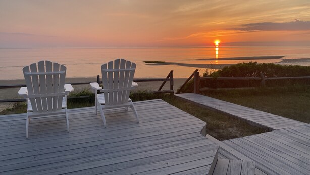 Two Adirondack chairs on a wooden deck overlooking a sunset over the ocean. - Oceanfront w/Private Stairs to Beach and Spectacular Sunsets! (Eastham)