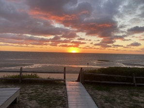 Une promenade en bois menant à une plage, avec un coucher de soleil en arrière-plan.