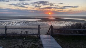 A wooden boardwalk leading to a beach with a sunset in the background. - Oceanfront w/Private Stairs to Beach and Spectacular Sunsets! (Eastham)