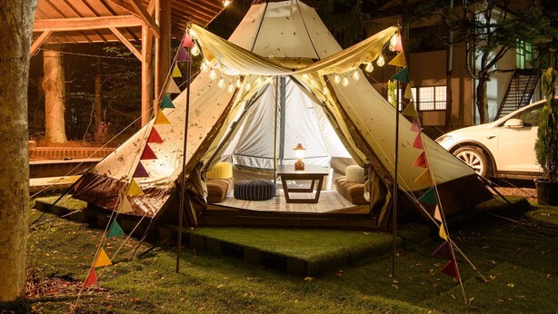 A tent with a table and chairs set up inside, surrounded by colorful triangular flags and string lights. - Ikoisanso (Karuizawa)