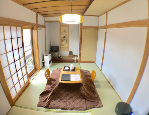 A traditional Japanese room with tatami flooring, a low table with a cushion, and a television in the background. - Ikoisanso (Karuizawa)
