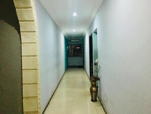 A narrow hallway with a tiled floor, a potted plant, and a door at the end.