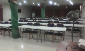 A conference room with rows of tables and chairs, a ceiling fan, and a projector.