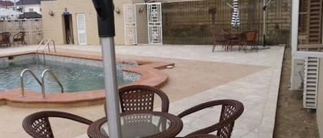 An outdoor pool area with a covered seating area and a poolside chair.