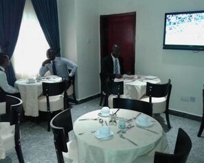 A conference room with round tables, chairs, and a projector screen on the wall. - Newcastle Hotel Lekki (Lagos)