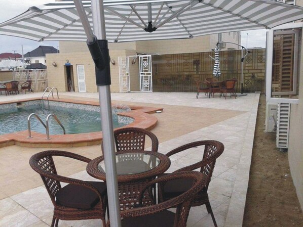 Relax by the pool in a serene outdoor space with a patio, wicker furniture, and a striped umbrella.