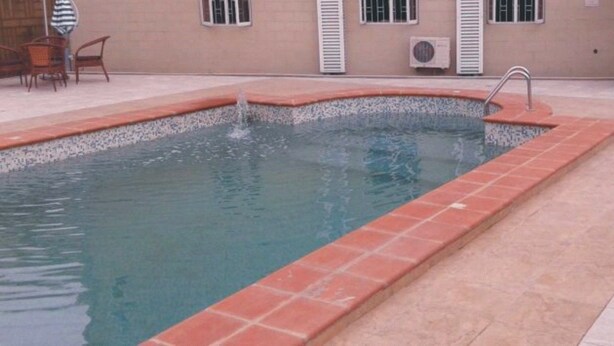 A rectangular swimming pool with a tiled edge, surrounded by a tiled patio area. - Newcastle Hotel Lekki (Lagos)