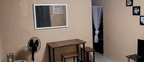 Uma sala de estar com ventoinha no teto, uma mesa com cadeiras, um sofá, um rack para TV e uma janela com cortina.