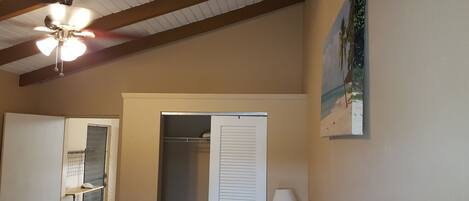 A room with a ceiling fan, a door leading to a closet, and a painting of a beach scene on the wall.