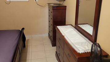 Une chambre à coucher comprenant un lit, une commode, un miroir, un téléviseur et un appareil de climatisation.