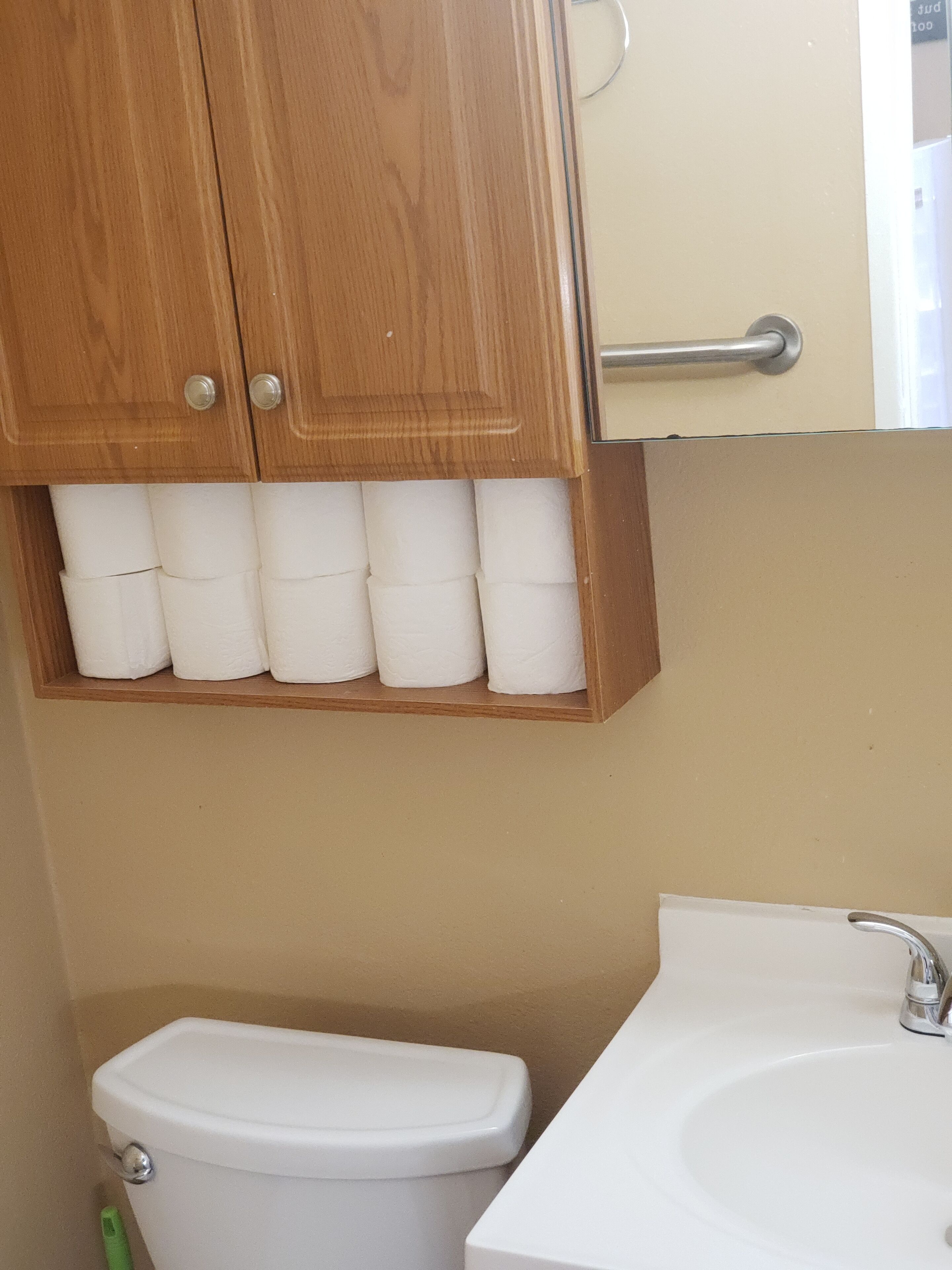 Un baño con un mueble de madera que contiene papel higiénico, un inodoro blanco y un lavabo con grifo.