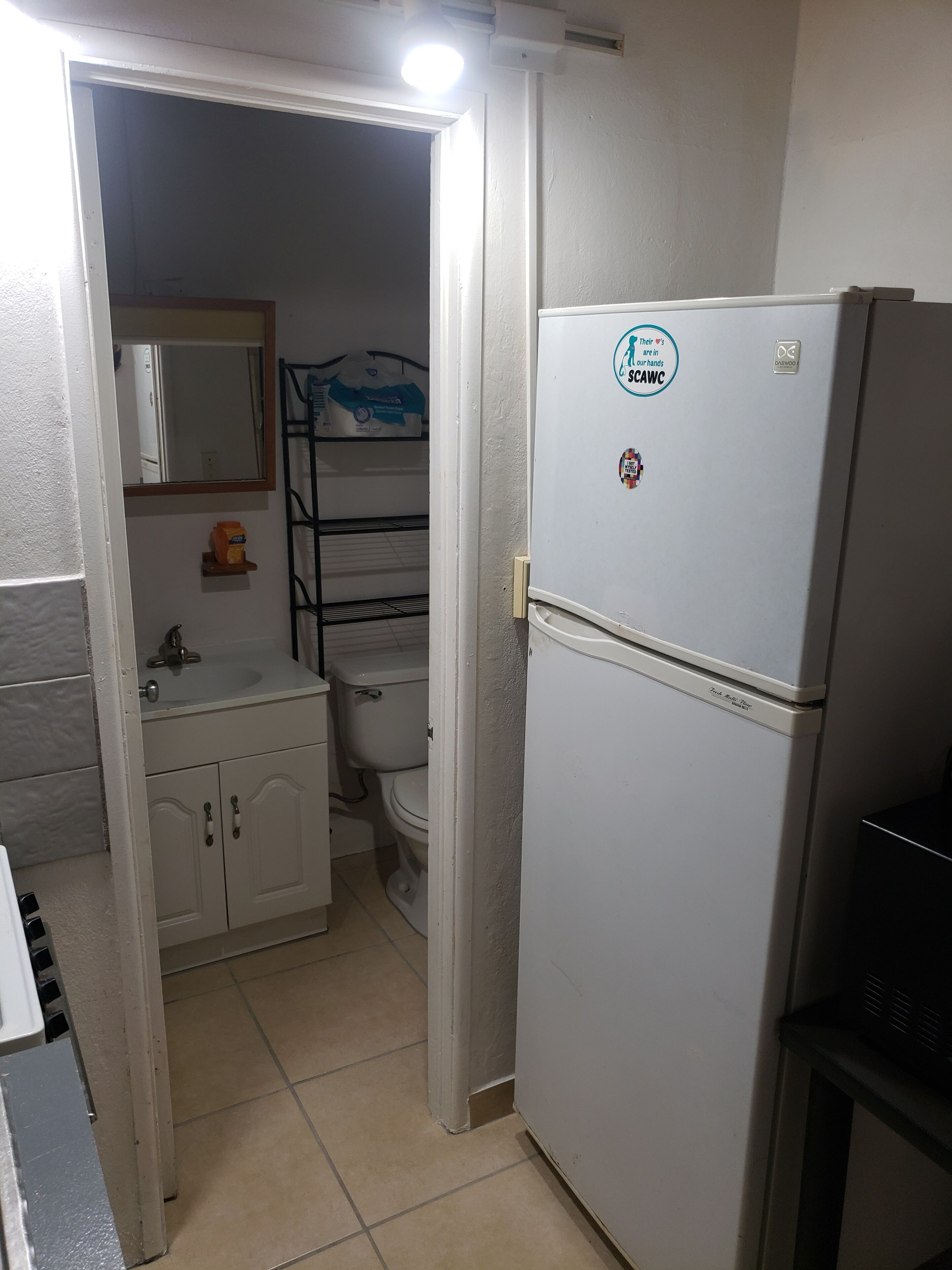 A compact kitchen with a refrigerator, a sink, and a toilet visible through an open door.
