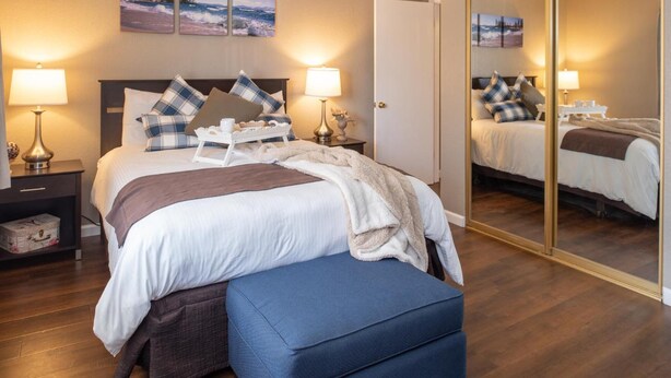 A hotel room with a bed, bedside tables, a mirror, and artwork on the wall. - Thunderbird Resort Club (Sparks)