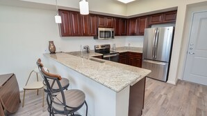 A modern kitchen with dark wood cabinets, stainless steel appliances, a granite countertop, and a bar stool. - Contemporary Urban Living in Gated Complex |2Q (Katy)