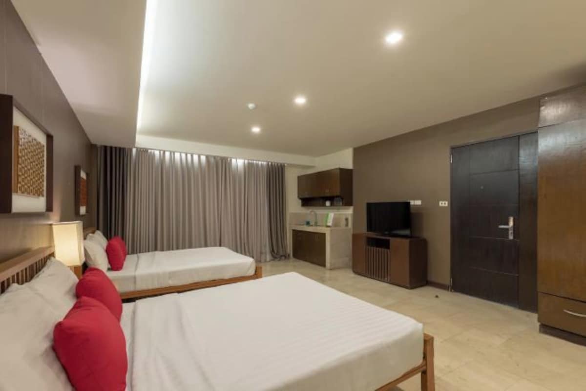 A hotel room with two beds, a kitchenette, a TV, and a wardrobe.