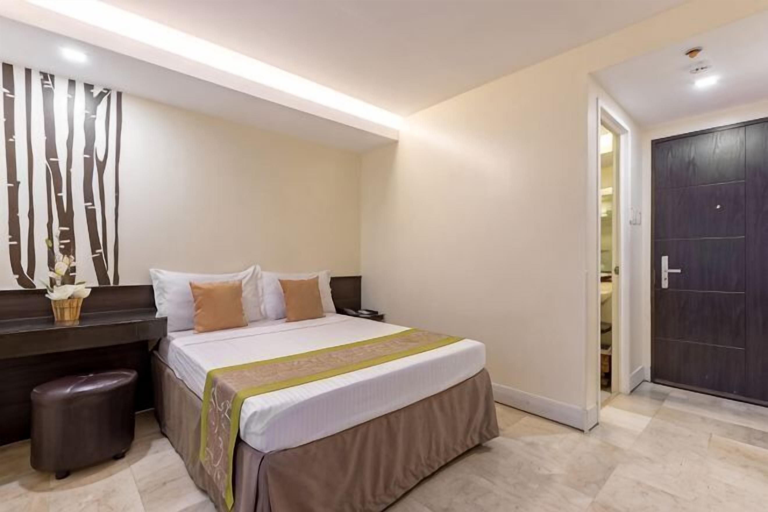 A bedroom with a bed, bedside tables, a nightstand, a dresser, and a door.