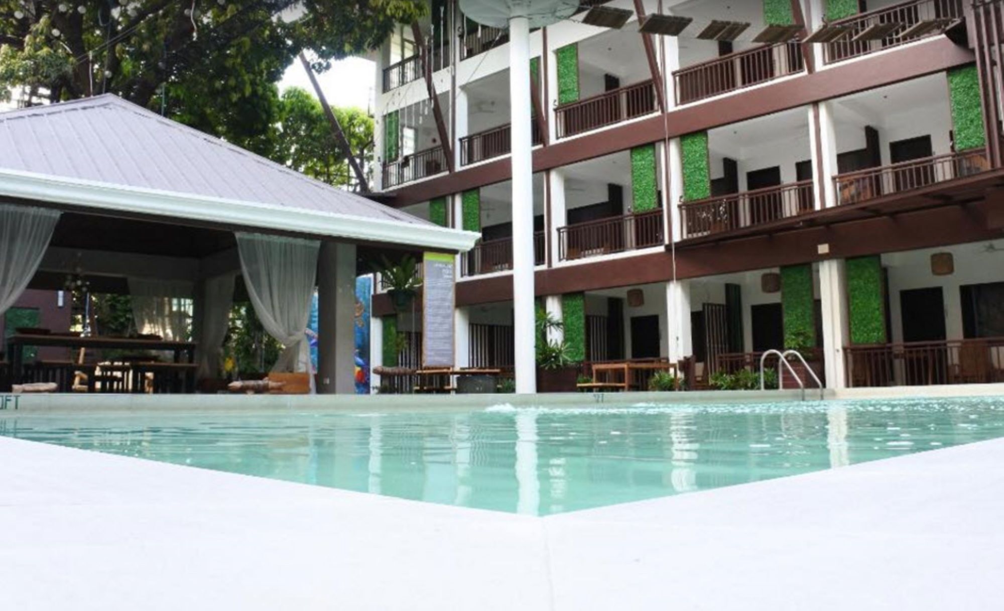 Un hotel de varios pisos con piscina, mobiliario exterior y balcones.