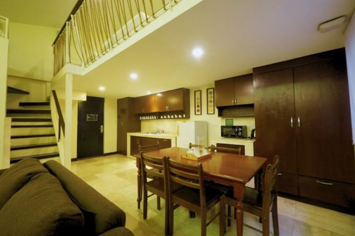 A dining area with a wooden table and chairs, a kitchen with dark cabinets, and a staircase leading to an upper level.
