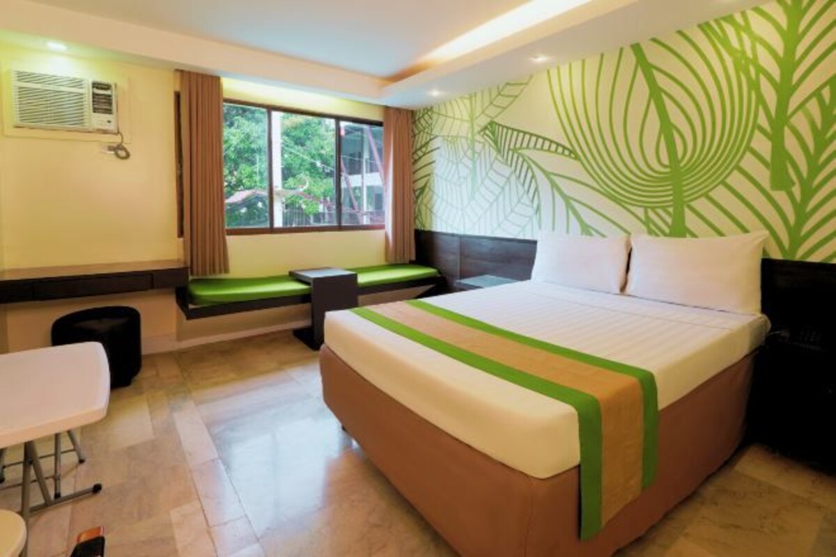 A hotel room with a bed, a bench, a table, and a window with a view.