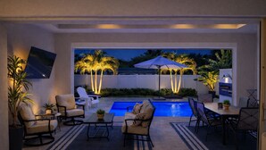 A modern outdoor patio with a pool, seating, and palm trees. - Enjoy a new construction home with heated salt pool close to everything Naples (Naples)