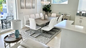 A modern kitchen with white cabinetry, a central island, and a dining area with white chairs and a wooden table. - Enjoy a new construction home with heated salt pool close to everything Naples (Naples)
