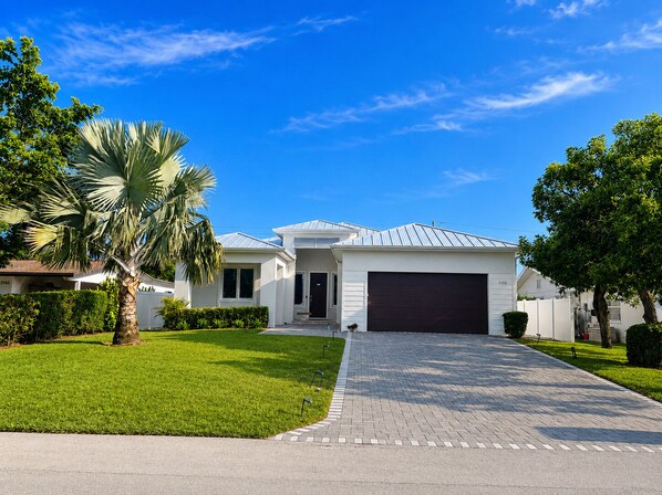 A modern single-story house with a garage, surrounded by well-maintained lawns and palm trees. - Enjoy a new construction home with heated salt pool close to everything Naples (Naples)