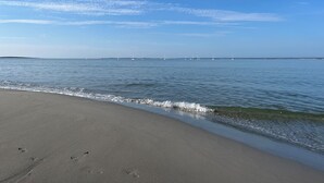 En strand med klar himmel, stilla vatten och en kustlinje som ligger en bit bort.