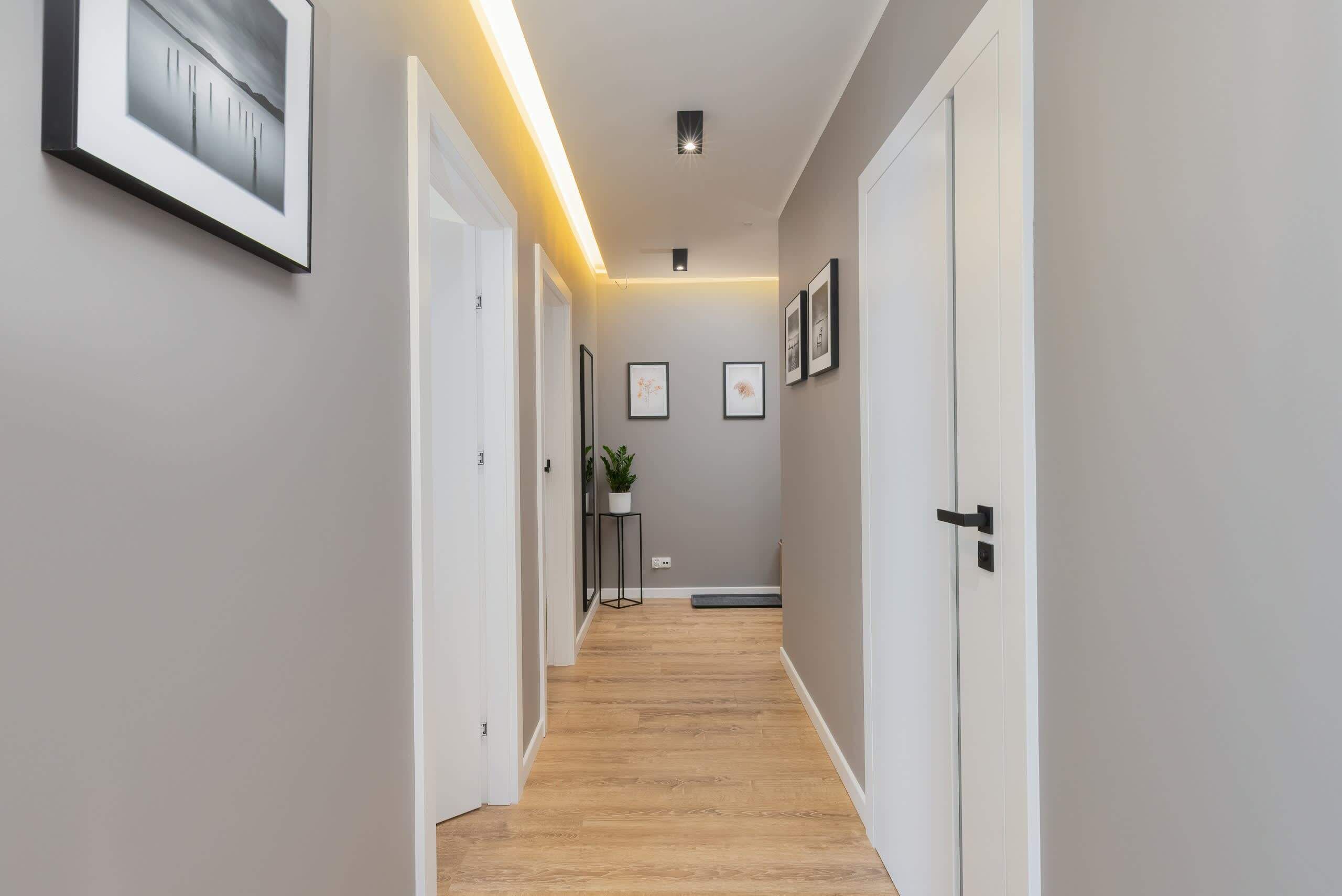 Un pasillo con piso de madera, paredes blancas y cuadros enmarcados.