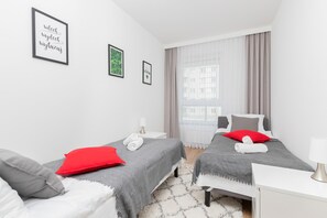 A modern hotel room with two beds, a white desk, and a large window with curtains.