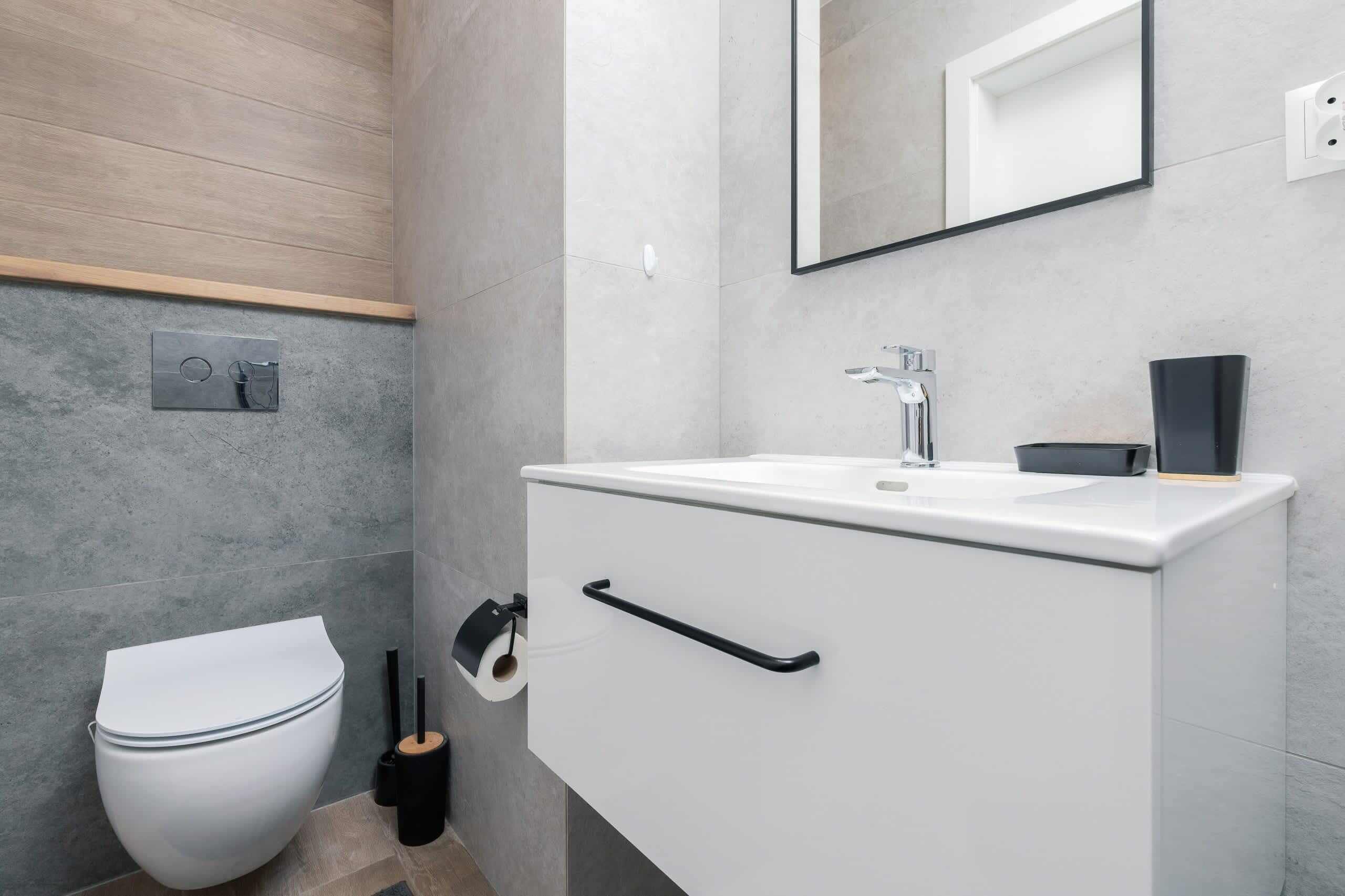 A modern bathroom with a white toilet, a sink with a mirror above it, and a wooden shelf.