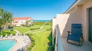 Un balcon avec vue sur une piscine, un terrain de golf et un bâtiment doté d’un toit rouge.